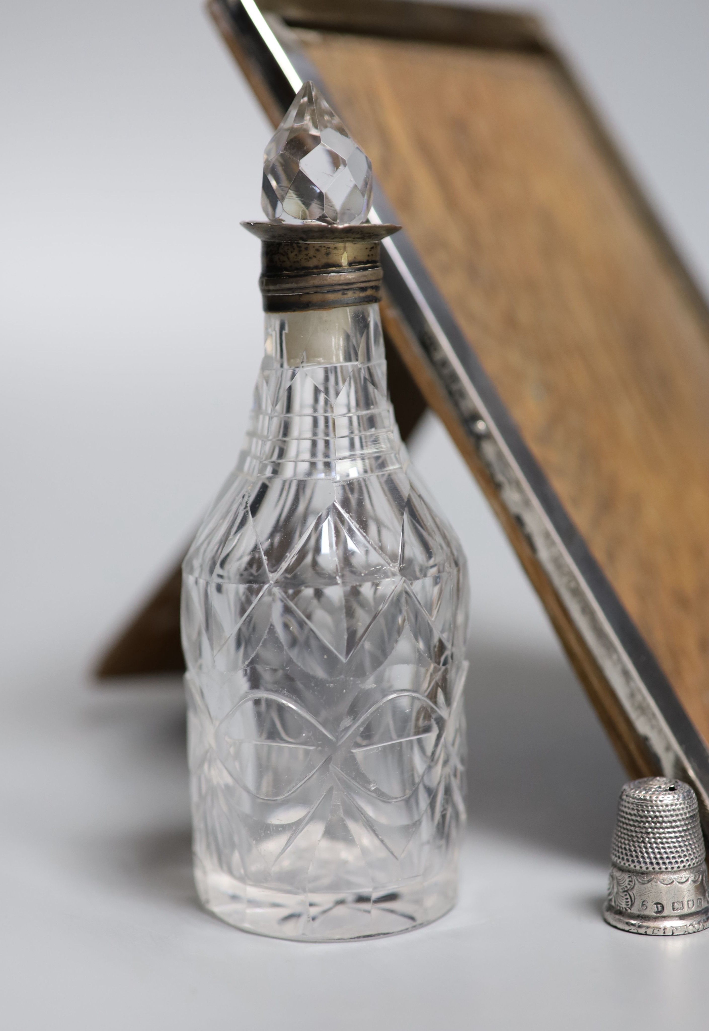 A silver mounted cigarette box, a silver mounted photograph frame, a silver thimble, a silver mounted comb(a.f.) and a silver mounted glass condiment bottle.